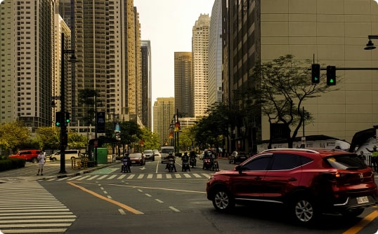 A red car driving down a city street, surrounded by tall buildings and bustling with activity, image